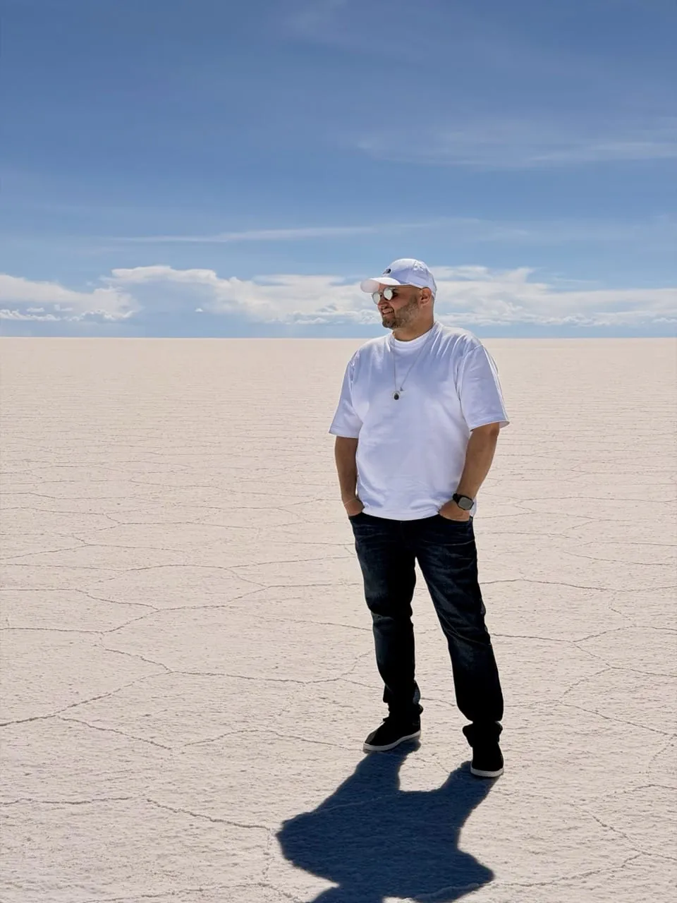 Hassan Elhassan standing on the vast white expanse of the Uyuni salt flats in Bolivia under a blue sky